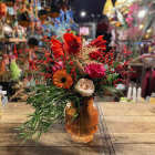 Prachtig kleurrijk boeket met rode en oranje bloemen, blauwe distels en gouden accenten, gepresenteerd in een glazen vaas op een houten tafel. 2