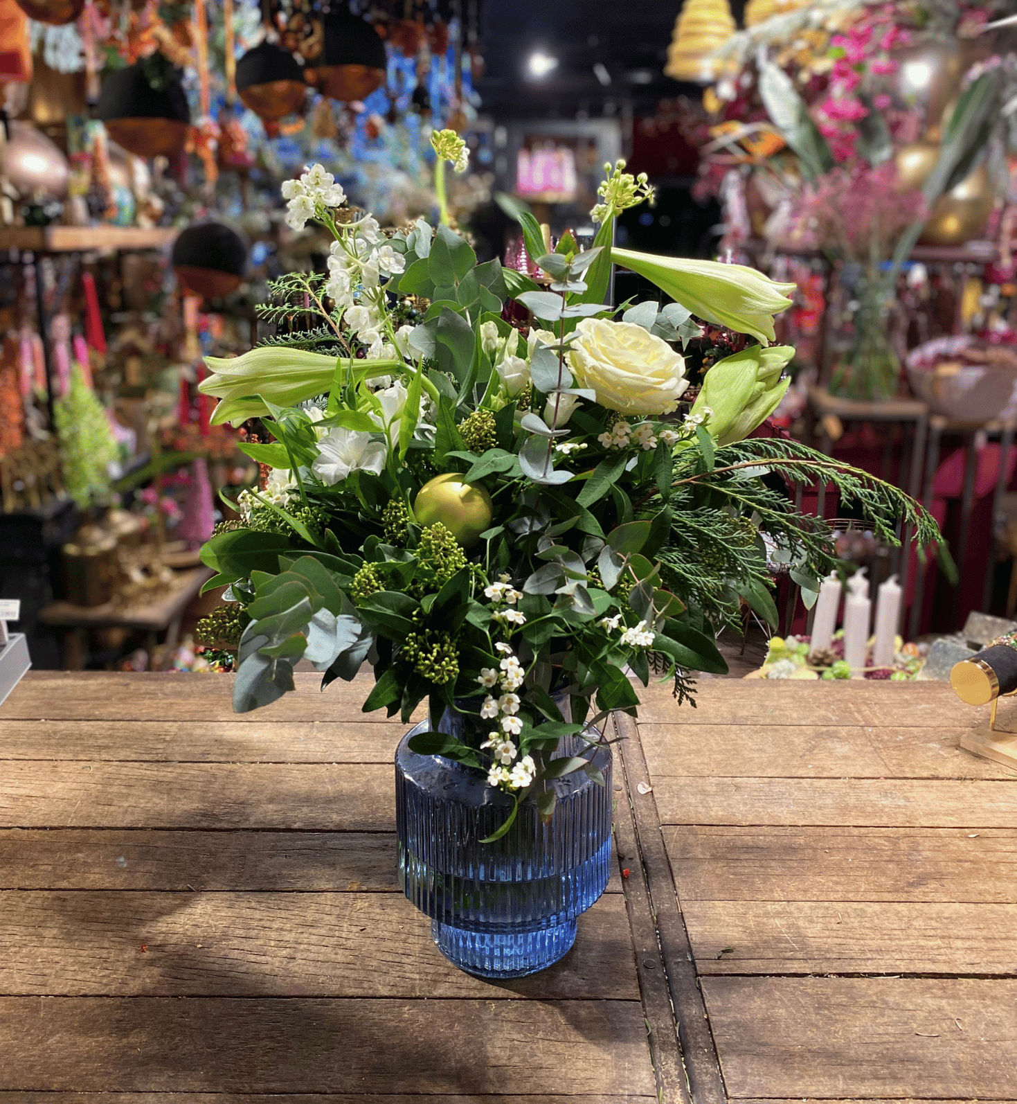 Fris boeket met witte rozen, lelies en groene accenten, stijlvol geschikt in een geribbelde blauwe vaas op een houten tafel.